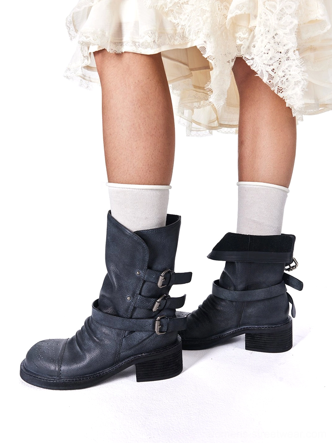Rear side view of distressed black leather triple-buckle ankle boots styled with white socks and lace skirt
