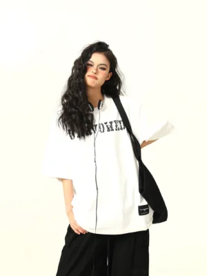 White distressed varsity letter oversized streetwear T-shirt styled with black wide-leg pants and shoulder bag