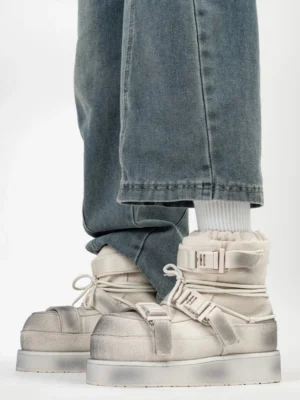 Distressed white triple-buckle platform snow boots worn with blue jeans and white socks, front view showing fleece lining, laces and thick sole