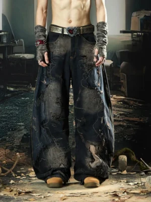 Front view of ultra-wide distressed denim pants in a faded dark wash styled with fingerless gloves and a statement belt in an industrial streetwear setting