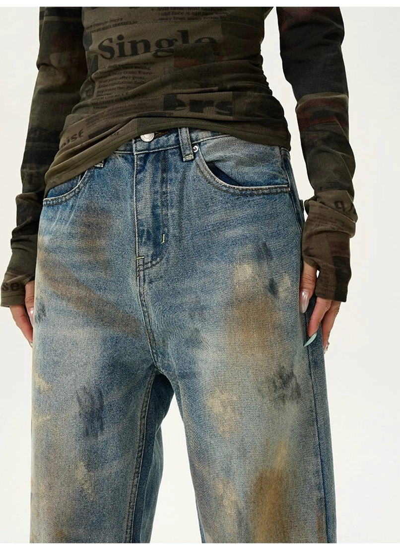 Close-up of distressed wide-leg jeans showing button waistband, belt loops, front coin pocket, and washed stained denim texture