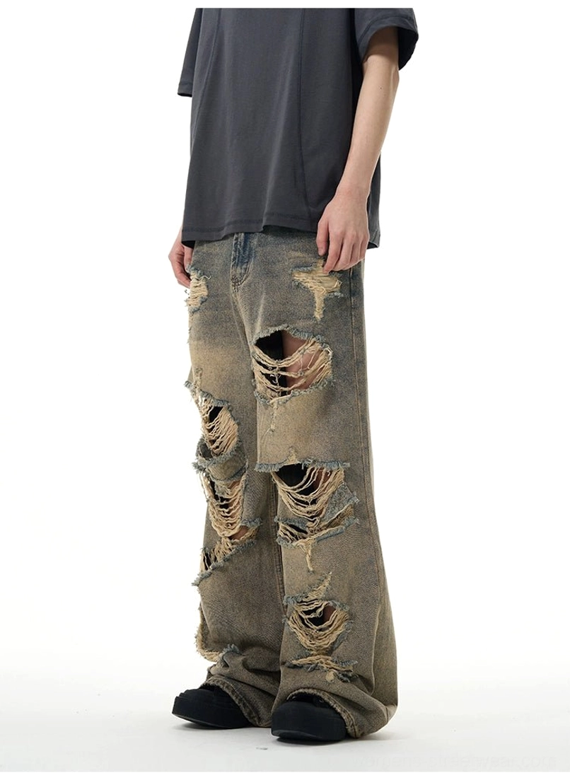 Side view showing the loose wide-leg silhouette, thigh rips, lower-leg distressing, and raw denim texture