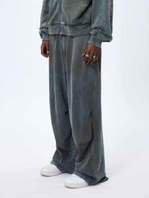 Front three-quarter view of faded gray distressed wide leg sweatpants styled with white sneakers in a minimalist streetwear studio