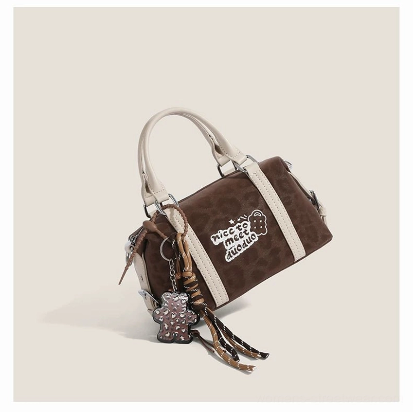 Rear angled view of a dark brown leopard Doodle Charm barrel bag with contrast trim, top handles and metal pendant tassel