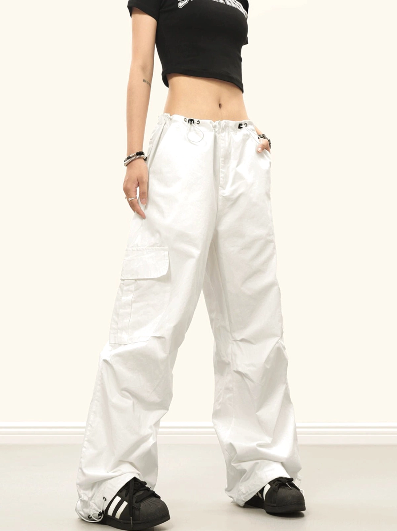 White baggy streetwear cargo pants with wide legs, side cargo pockets, drawstring waist and adjustable ankle cuffs shown in a front three-quarter outfit view