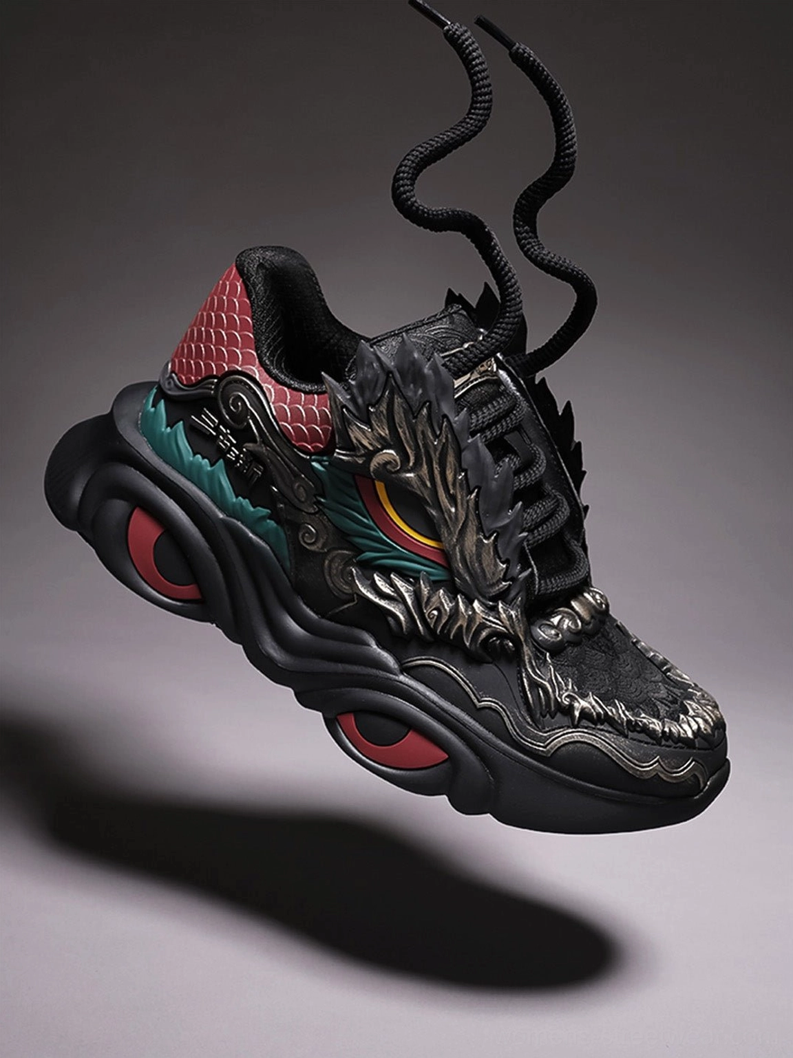 Close-up front three-quarter view of black dragon sneakers with a full dragon head vamp ornament, exposed laces, teal midfoot stripe, and red sole inserts