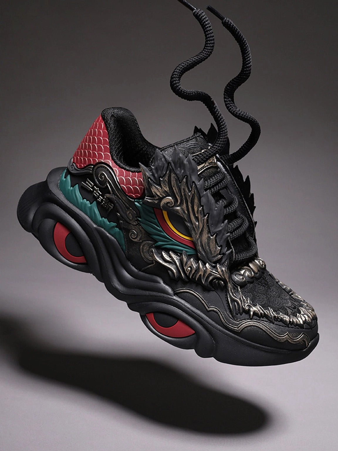 Front three-quarter view of black dragon crest sneakers with lace-up construction, dragon head ornament, colorful eye details, and thick cushioned sole