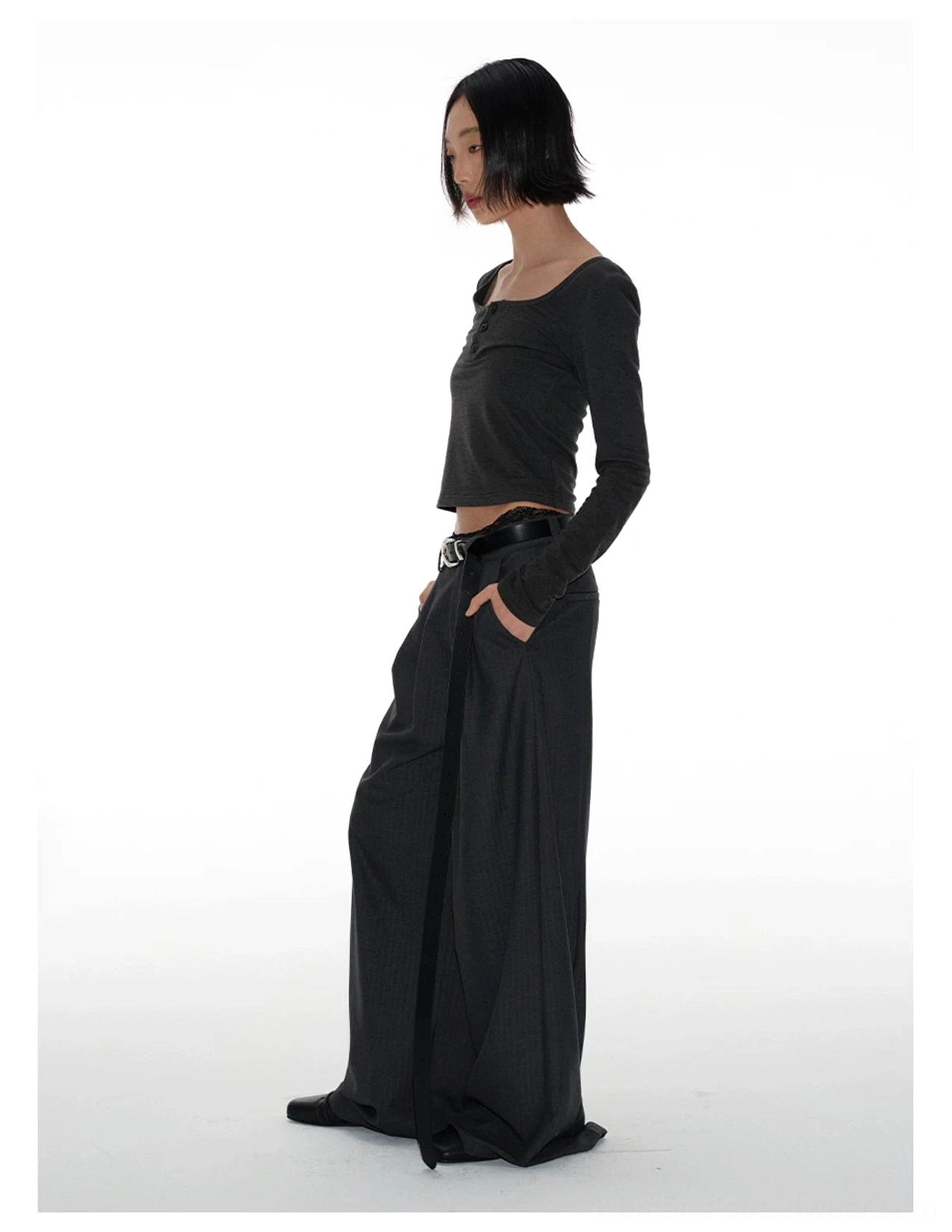 Side view of draped charcoal wide-leg streetwear trousers with a black waist belt, clean side seams, and fluid tailored movement