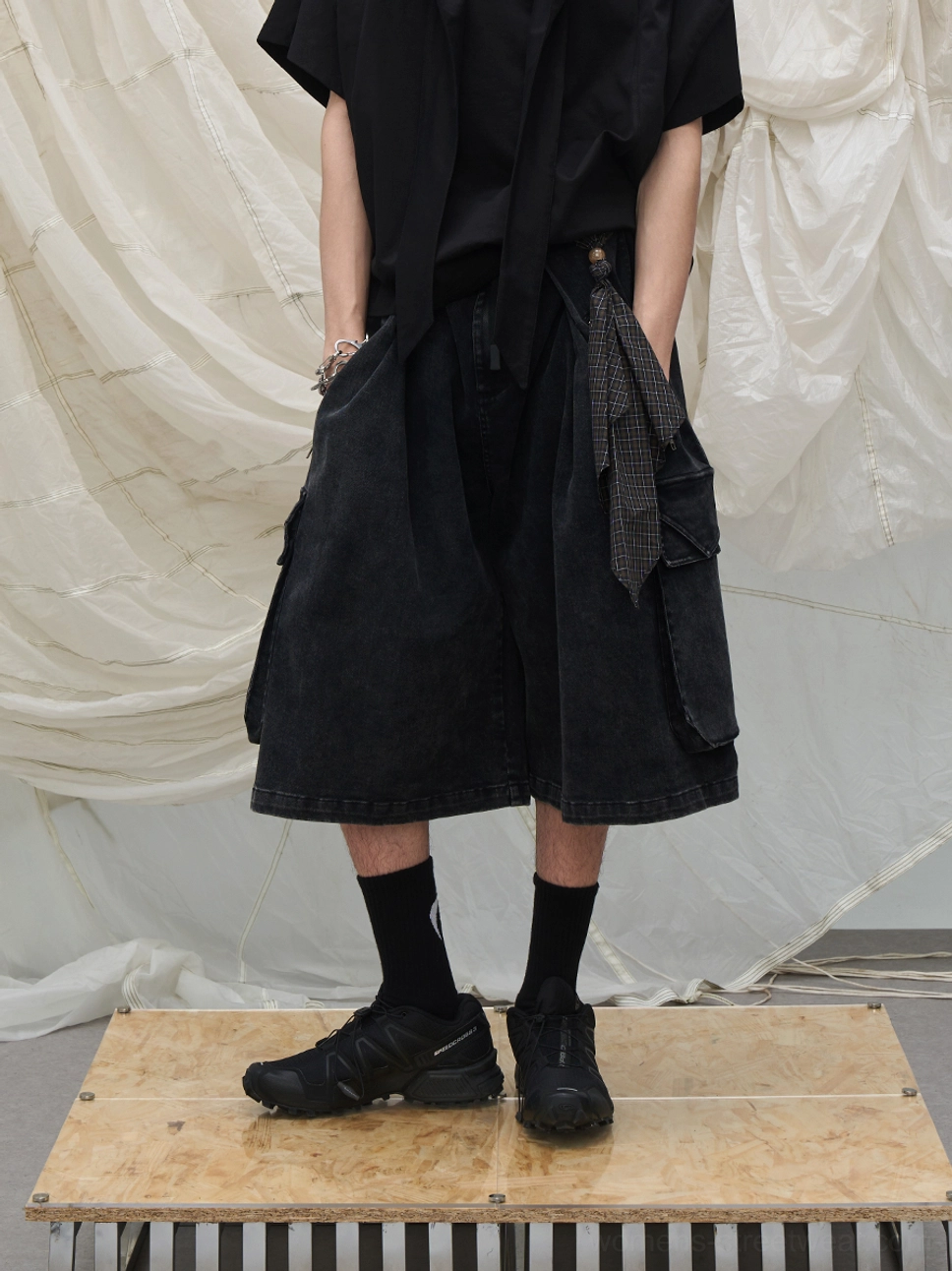 Black washed cargo culotte shorts with multiple utility pockets, layered scarf trims, and oversized streetwear silhouette