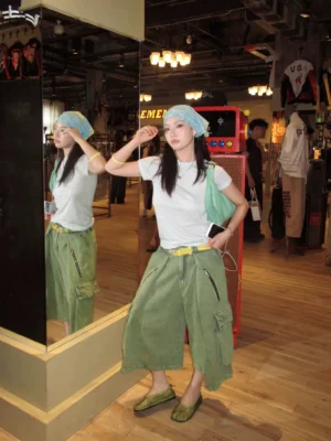 Washed green cargo culotte shorts with oversized wide legs, utility pockets, yellow waist belt, and layered streetwear styling