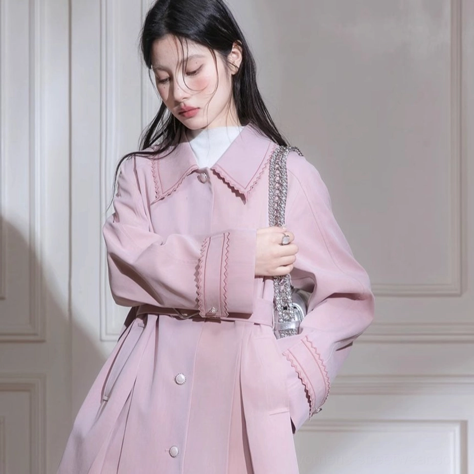 Dusty pink belted trench coat with scalloped cuffs styled over a white turtleneck in an indoor studio