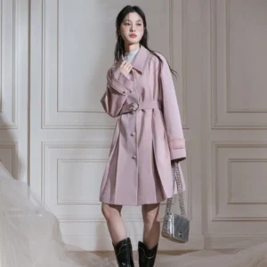 Full front view of dusty pink belted trench coat with pleated A-line hem and black ankle boots