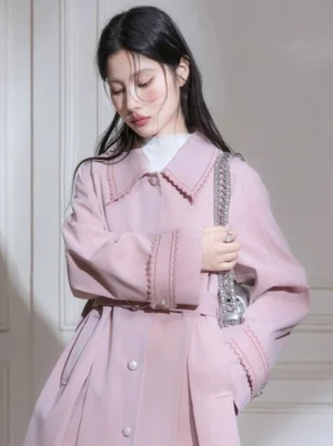 Dusty pink scalloped collar pleated hem belted trench coat worn with a white turtleneck and silver chain handbag