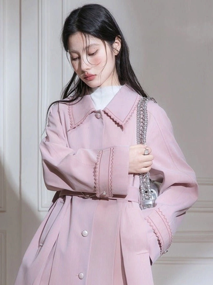 Dusty pink scalloped collar pleated hem belted trench coat worn with a white turtleneck and silver chain handbag