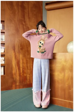 Dusty pink vintage bunny knit sweater styled with patchwork trousers in a retro study, featuring green and pink ribbed trim and a cute kawaii streetwear graphic