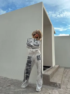 Full early-2000s grunge tracksuit styling with washed gray wide-leg streetwear pants, black racing stripes, slogan graphics, and matching retro sport outerwear