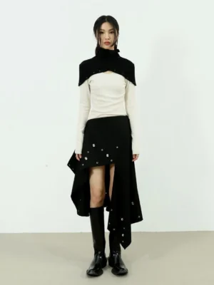 Full body front view of two-tone high-neck knit top styled with an asymmetric black skirt and ankle boots