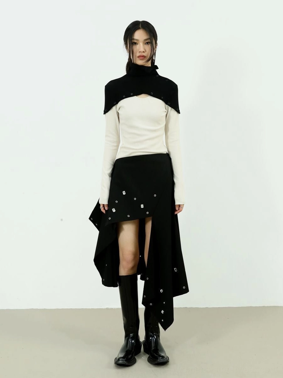 Full body front view of two-tone high-neck knit top styled with an asymmetric black skirt and ankle boots