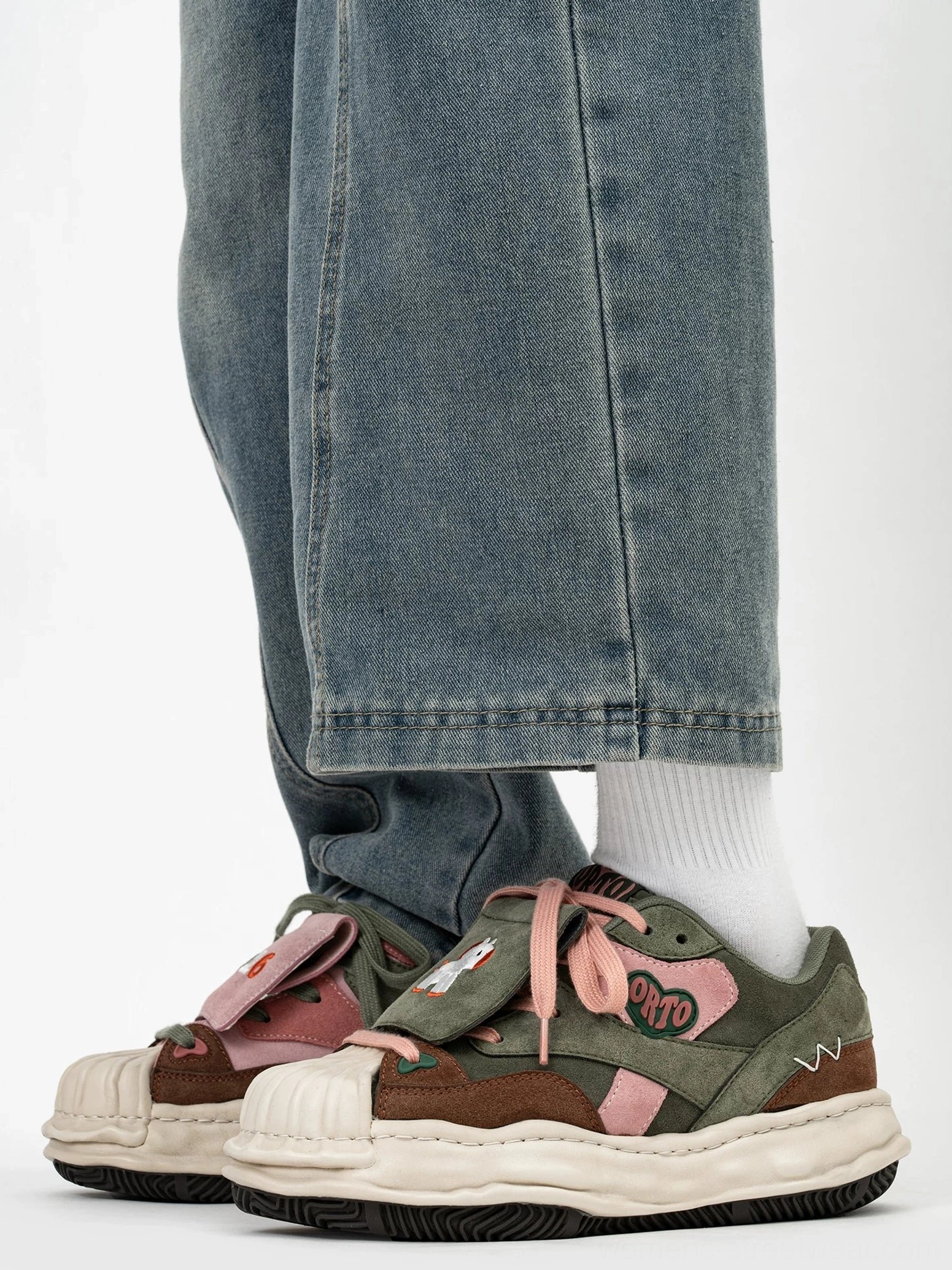 Front view of embroidered color block lift sneakers worn with denim jeans and white socks, featuring 2026 patch and cartoon detail