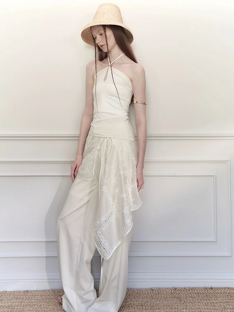 White embroidered wrap skirt wide-leg streetwear trousers styled with a halter top and straw hat in studio