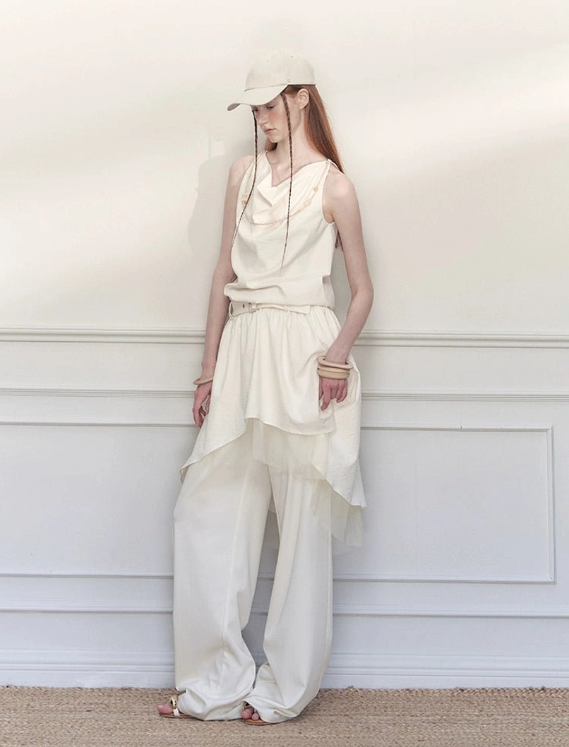 White asymmetric wrap skirt wide-leg trousers styled with a layered sleeveless top and baseball cap