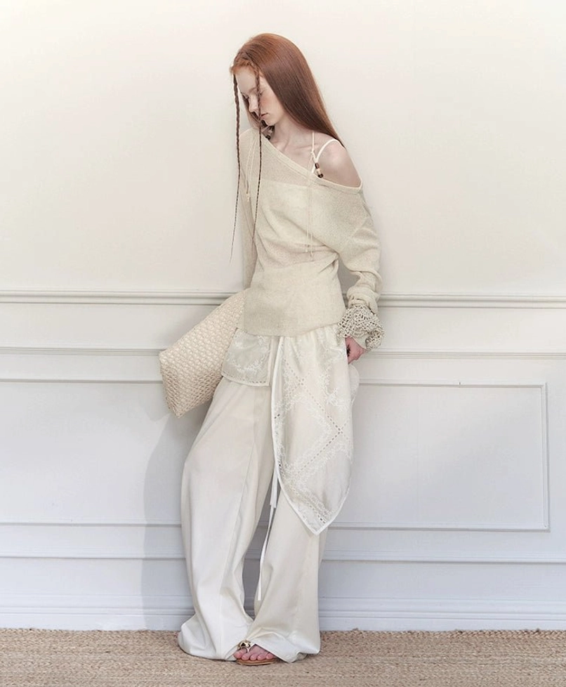 Side view of white embroidered wrap skirt wide-leg trousers styled with an off-shoulder top and woven straw bag