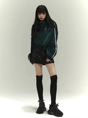 Emerald green satin track jacket styled with black leather hot shorts, over-the-knee socks, chunky sneakers, and contrast white sleeve stripes