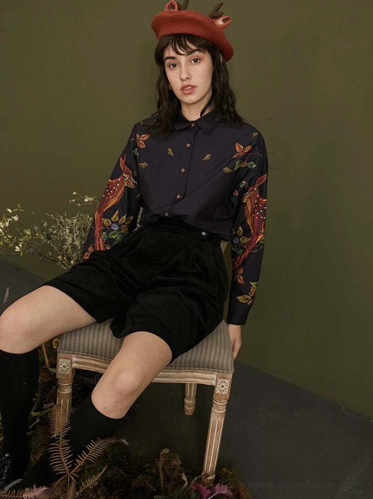 Seated model wearing enchanted forest deer and leaf print navy cotton button-up blouse with classic collar
