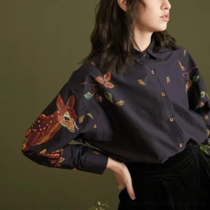 Side view of navy enchanted forest deer and foliage print cotton blouse tucked into high-waisted black pants