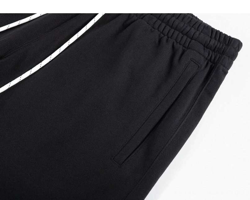 Close-up of black cotton sweat shorts waistband, dotted drawstring, stitched side pocket, and dense knit fabric