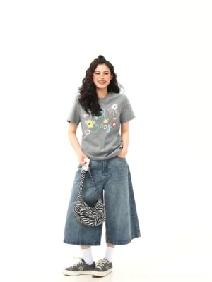 Full-body female model wearing gray floral graphic streetwear T-shirt with wide-leg cropped jeans, zebra shoulder bag, white socks, and vintage canvas sneakers