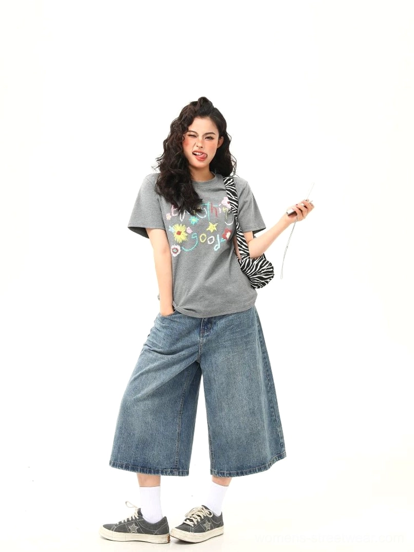 Full-body casual outfit featuring gray Everything Good floral graphic T-shirt, denim jeans, white crew socks, and vintage canvas sneakers