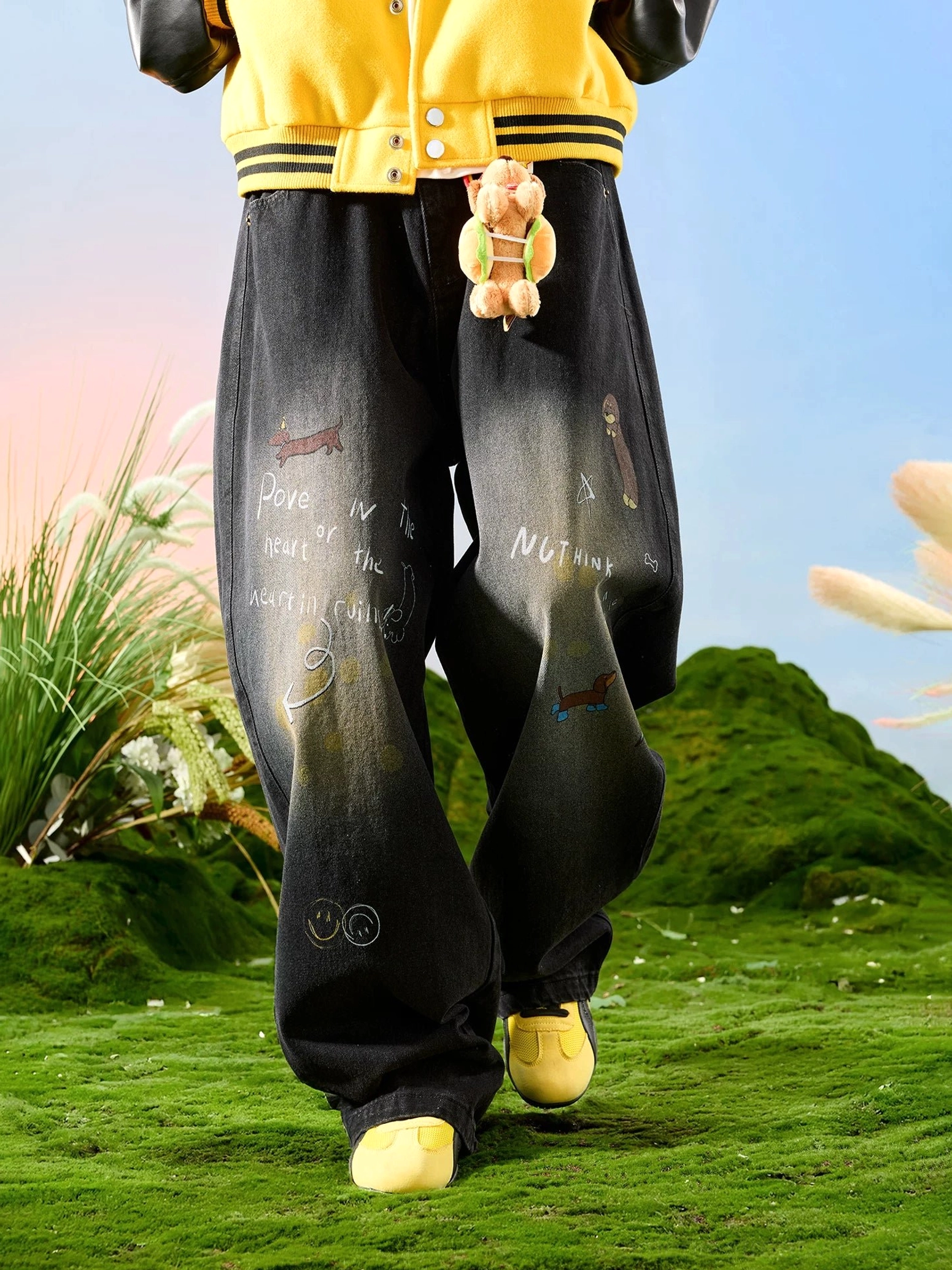 Three-quarter front view of faded black graphic wide leg jeans with teddy bear charm playful doodles and contemporary streetwear details