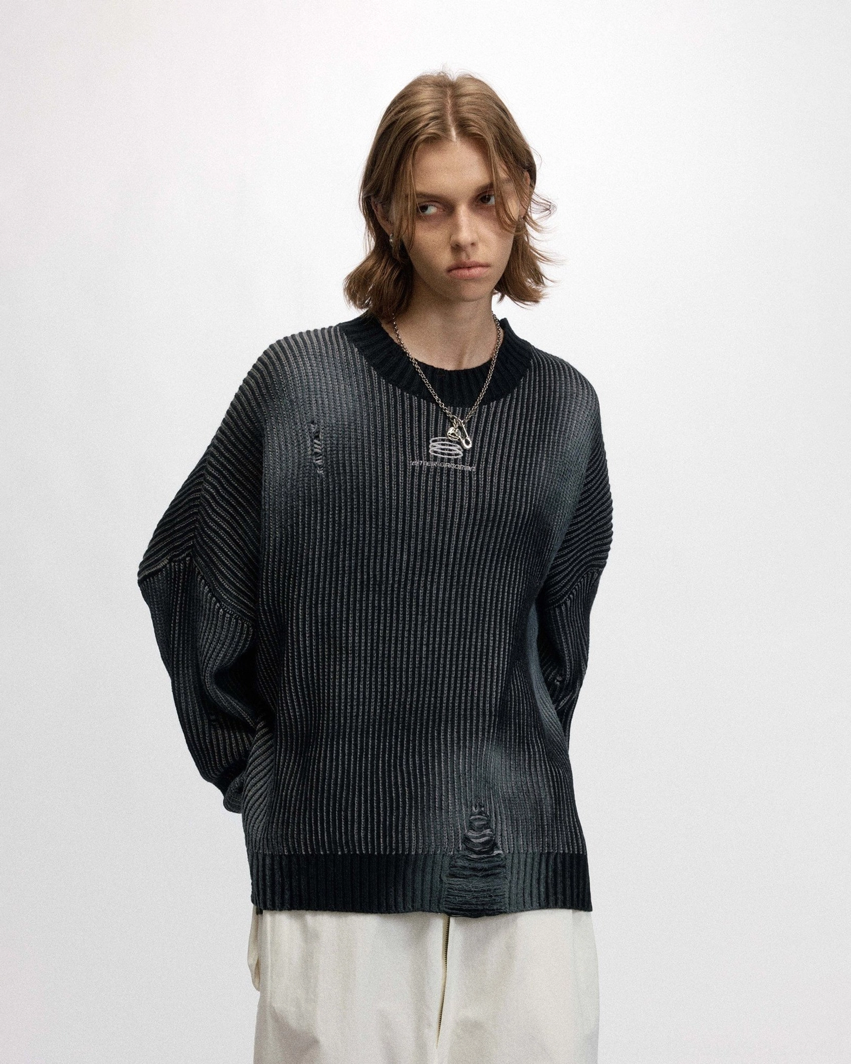 Close-up front view of a faded black ribbed logo sweater styled with layered necklace and white trousers