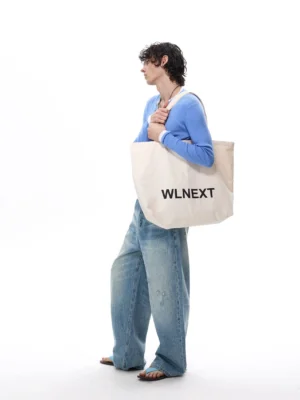 Three-quarter view of relaxed faded blue balloon jeans with wide legs styled with a blue cardigan and canvas tote