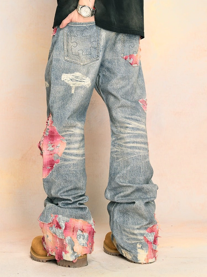 Front three-quarter view of faded blue distressed wide-leg jeans with pink frayed patches styled with a draped denim jacket and tan work boots