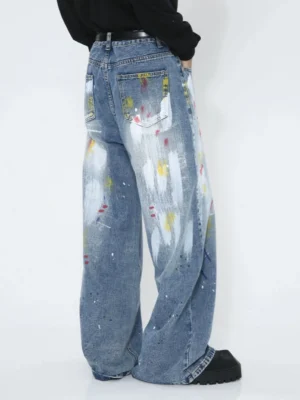 Rear low-angle view of faded blue wide-leg graffiti jeans with colorful paint splatter details, back pocket and relaxed streetwear styling