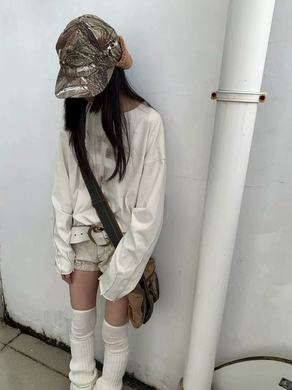 Female model side view wearing oatmeal gray faded cross long sleeve tee styled with denim shorts and leg warmers