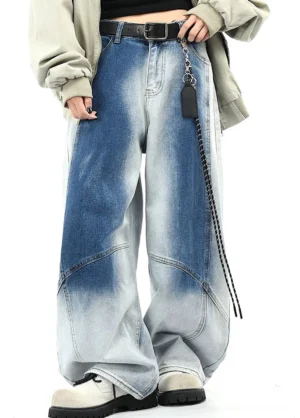 Front three-quarter view of blue faded wide-leg denim pants showing curved tailored seams, high-waisted streetwear silhouette, loose jacket, chain belt, and sneakers