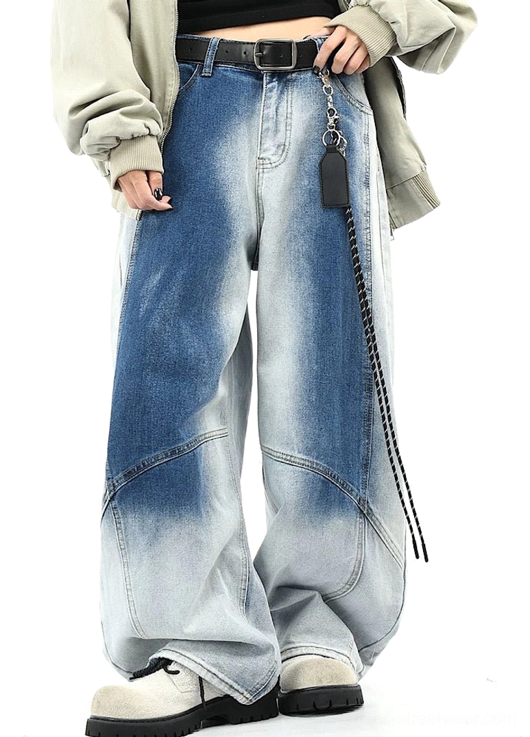 Front three-quarter view of blue faded wide-leg denim pants showing curved tailored seams, high-waisted streetwear silhouette, loose jacket, chain belt, and sneakers