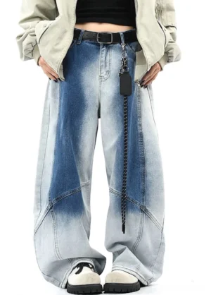 Front full-body view of faded blue wide-leg denim streetwear pants with gradient wash, curved panel seams, cropped top, loose outerwear, chain belt, and casual sneakers