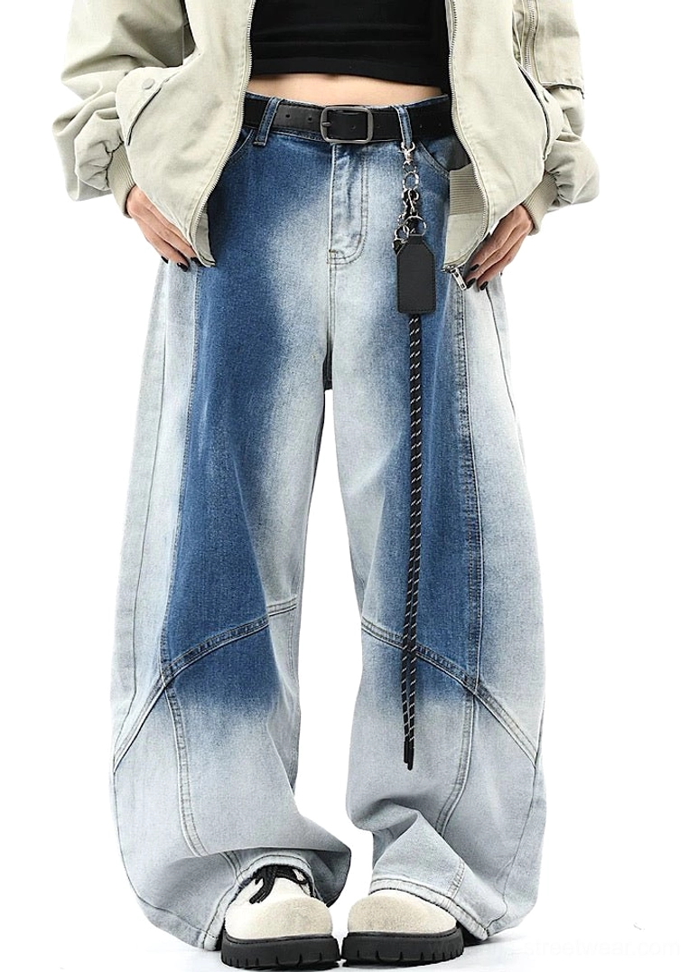 Front full-body view of faded blue wide-leg denim streetwear pants with gradient wash, curved panel seams, cropped top, loose outerwear, chain belt, and casual sneakers