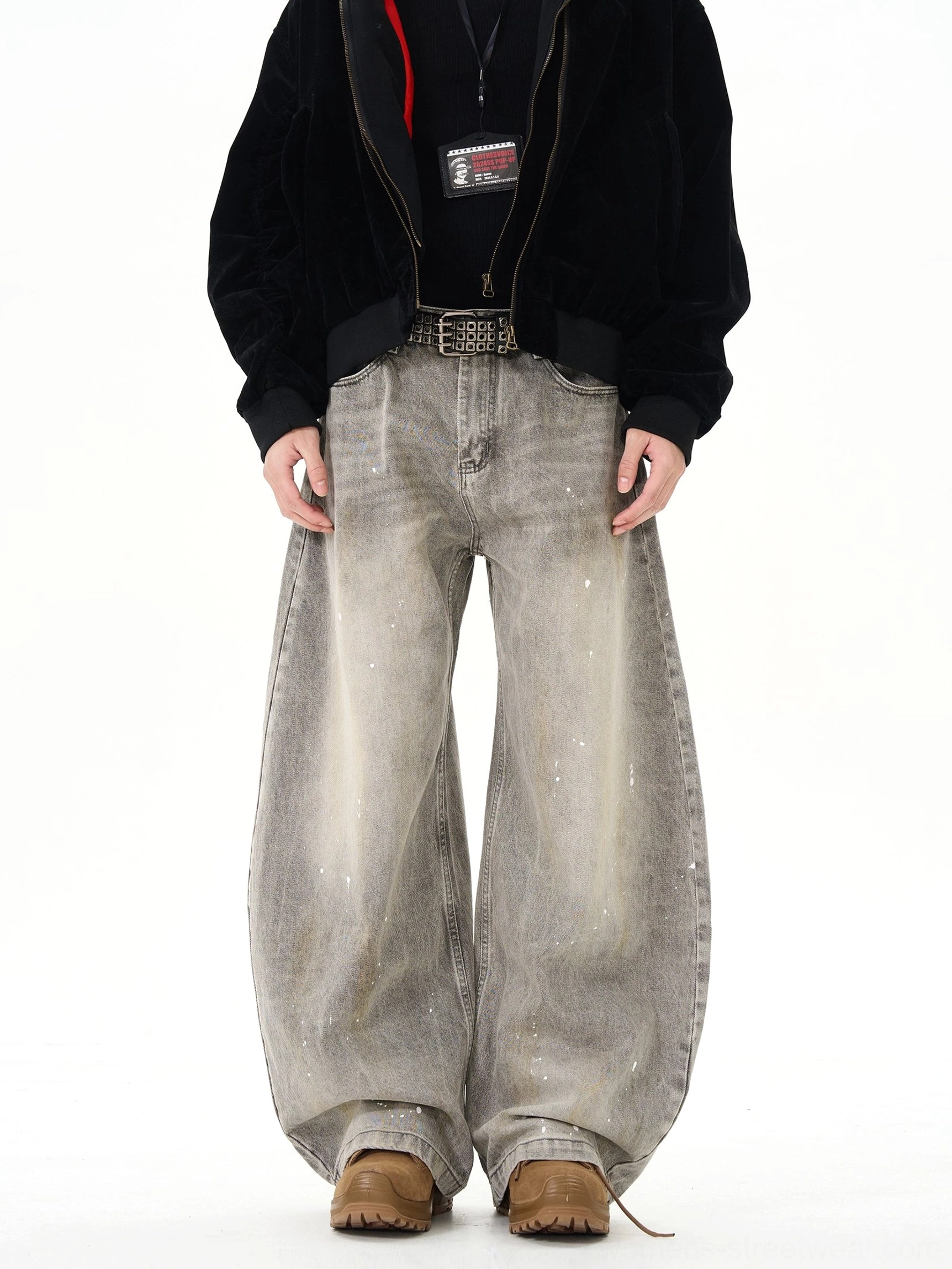 Male model wearing faded grey paint splatter wide leg jeans with brown loafers in white studio