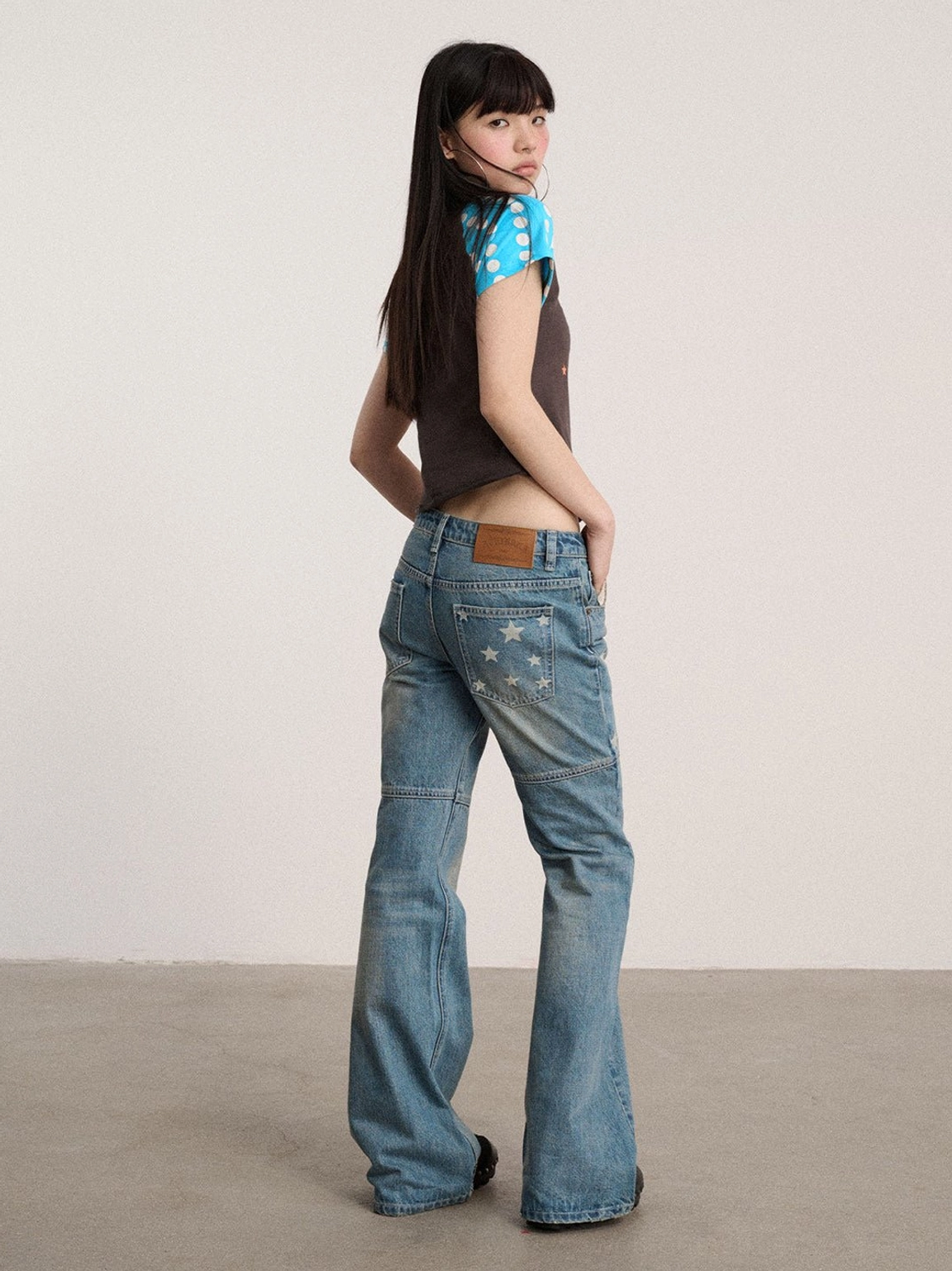 Back view of faded indigo low-rise flare jeans featuring back pocket star details, waistband tab, and bootcut hems
