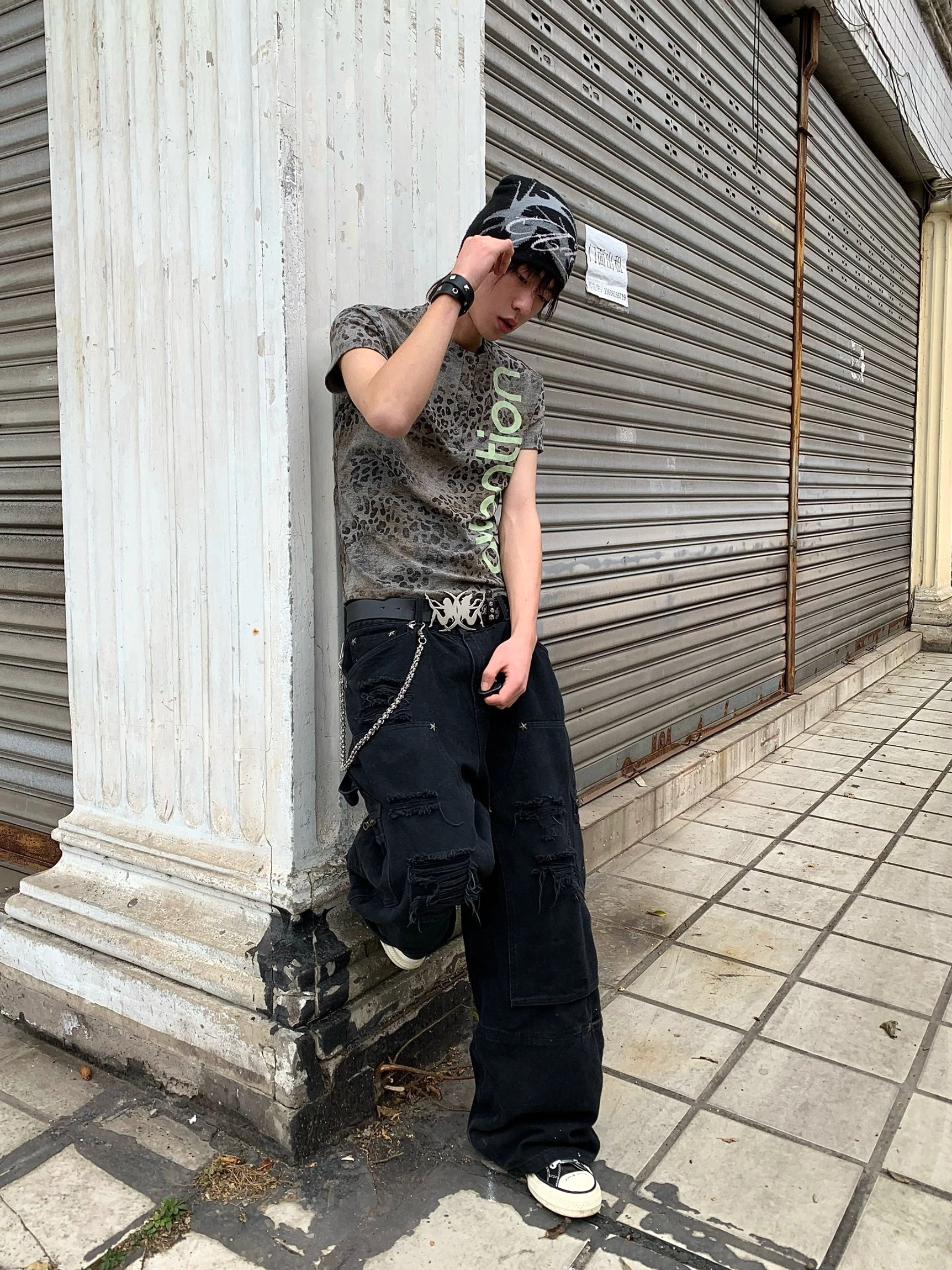 Side rear view of a faded leopard Henley streetwear tee worn with baggy black denim on a city street