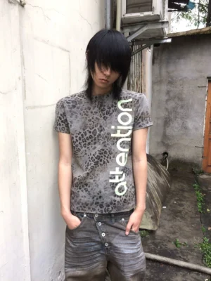 Front full-body view of a faded leopard print Henley tee with vertical lime turquoise attention graphic styled with vintage low-rise denim in an outdoor city alley