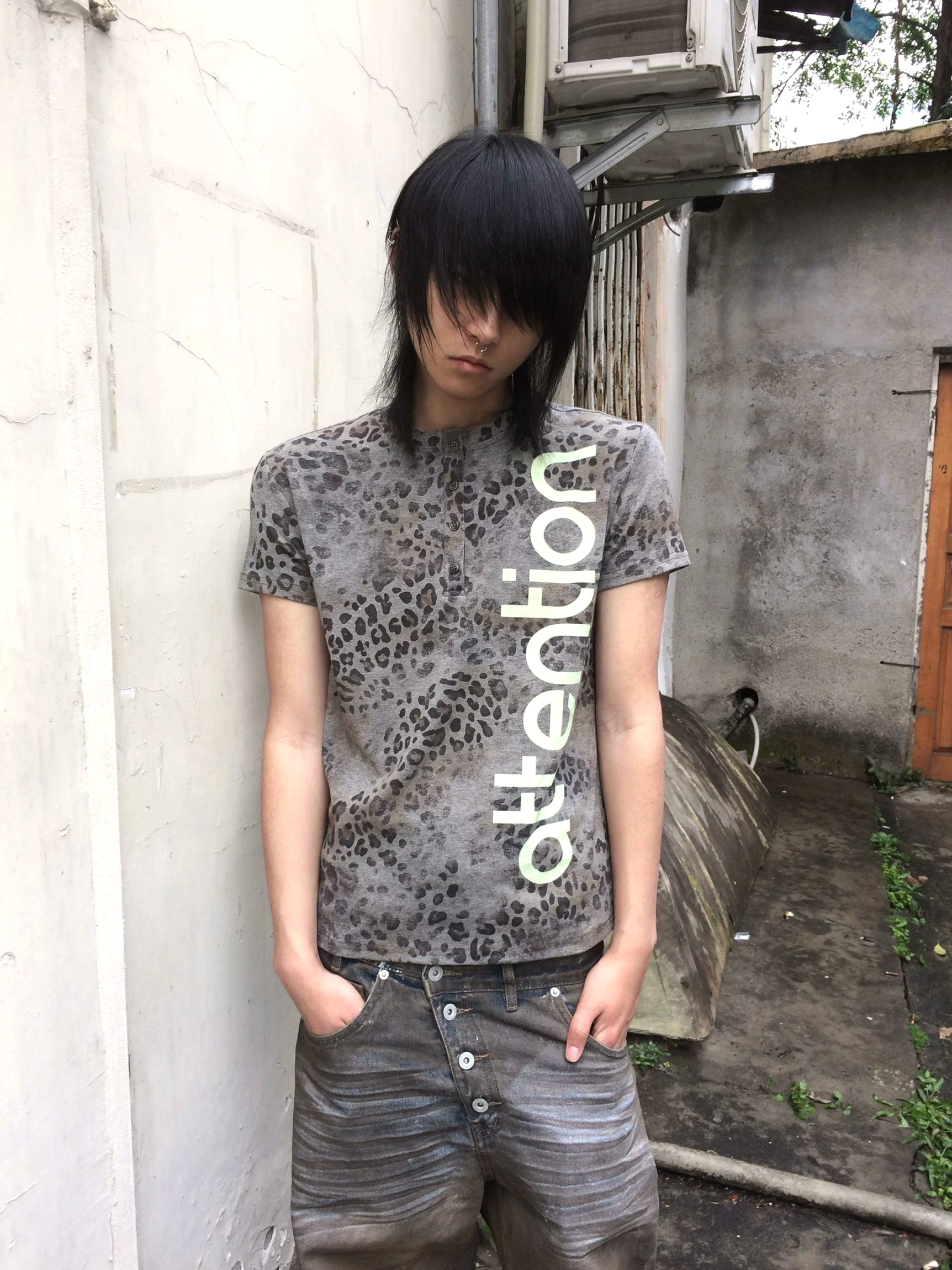 Front full-body view of a faded leopard print Henley tee with vertical lime turquoise attention graphic styled with vintage low-rise denim in an outdoor city alley