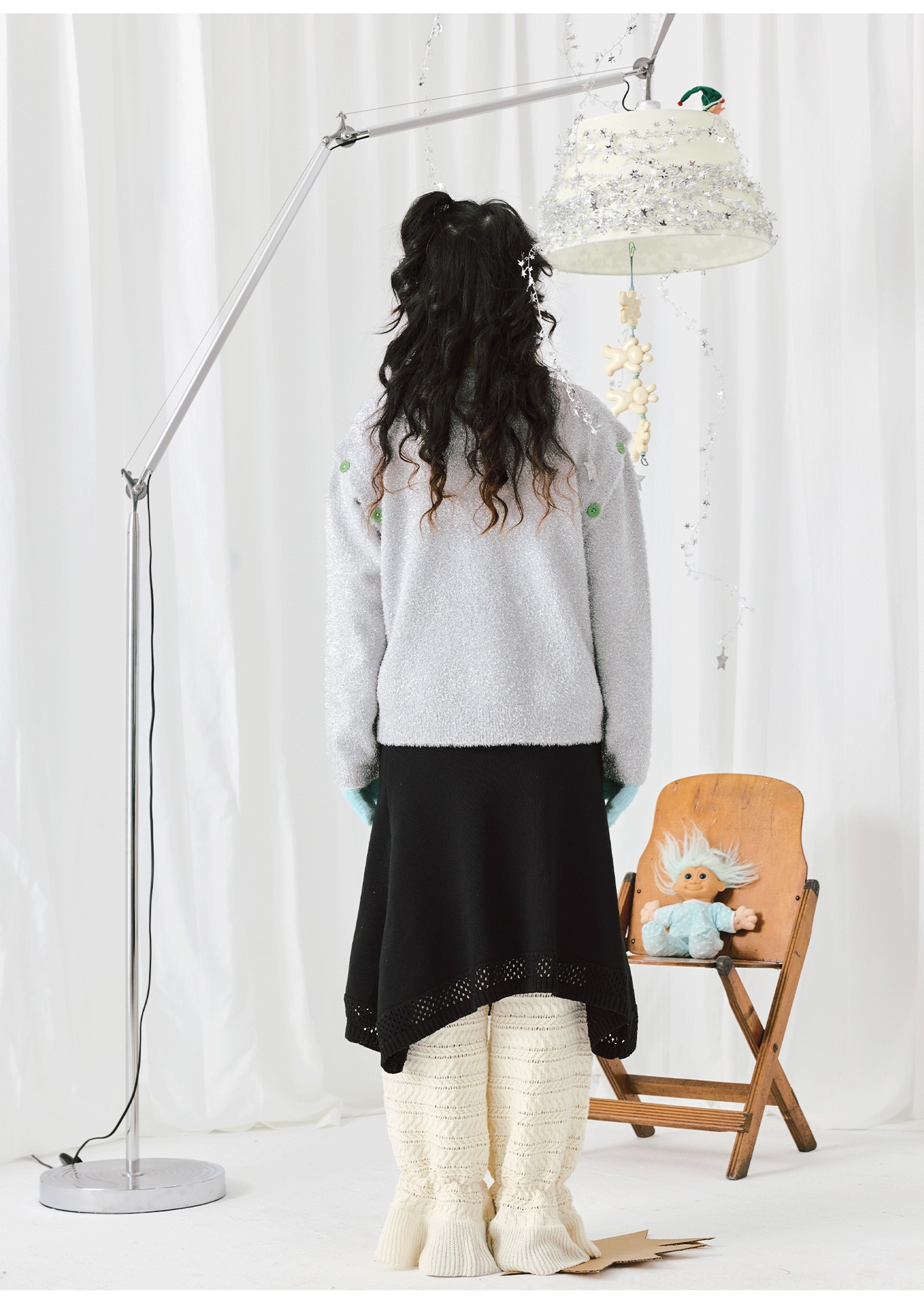 Back view of a silver-grey cartoon knit sweater showing its relaxed silhouette and green shoulder accents with a black midi skirt