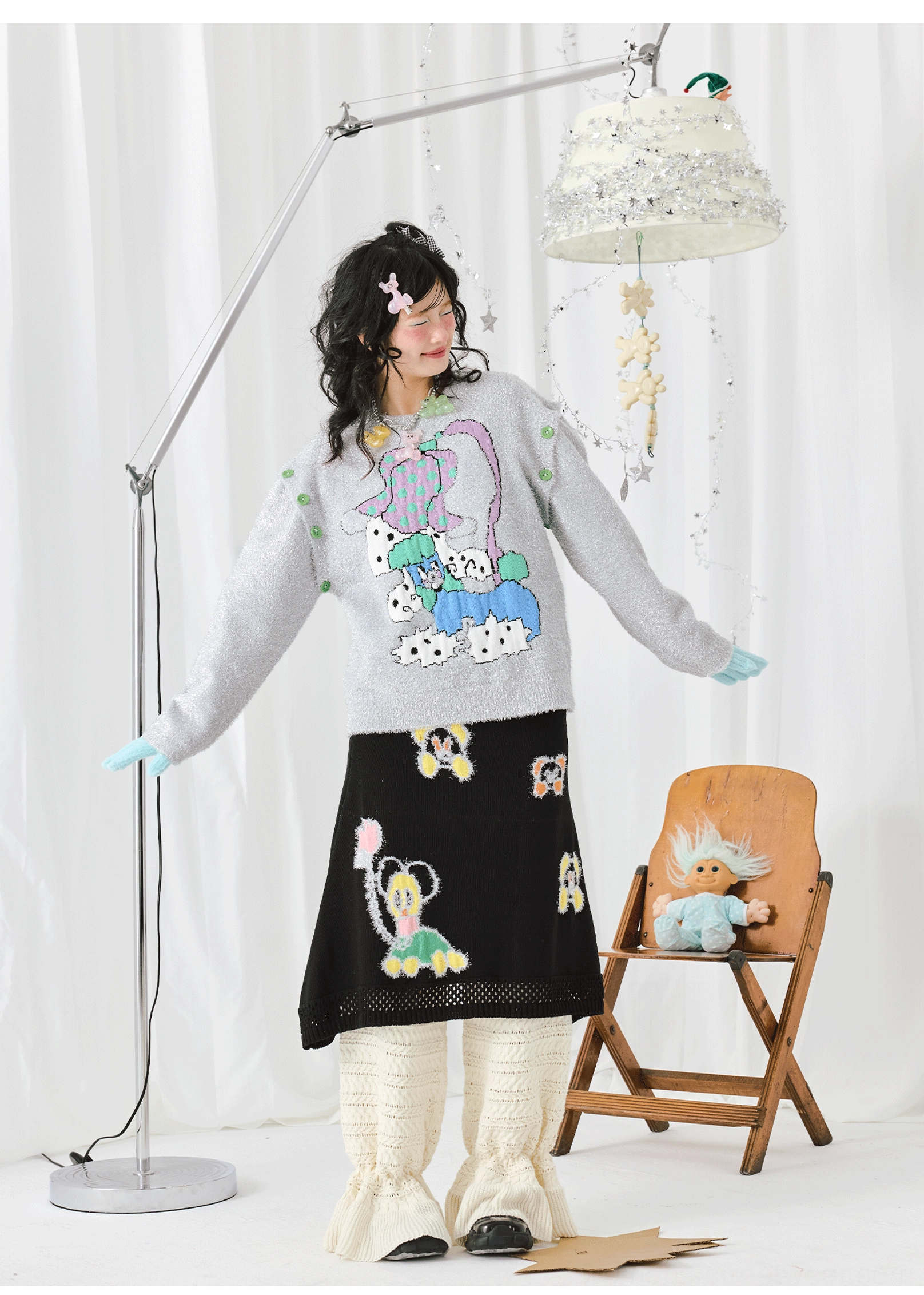 Three-quarter view of a relaxed silver-grey cartoon graphic knit sweater with colorful artwork and playful streetwear styling