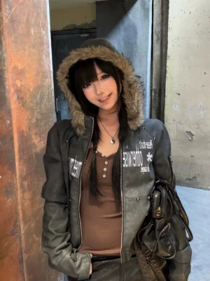 Front view of a cropped dark gray PU jacket with brown faux fur hood trim, graphic lettering, and avant-garde streetwear styling